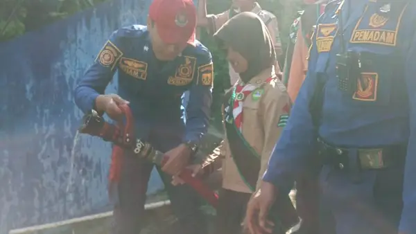 Pelajar sekaligus anggota Pramuka SD Margawangi Sukamaju, Kecamatan Sukalarang, Kabupaten Sukabumi, mencoba mengendalikan selang air bertekanan tinggi, didampingi petugas Damkar Sukaraja. | Foto: Istimewa