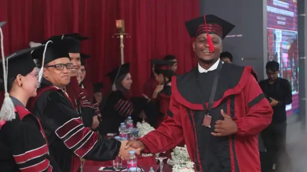 Momen Kudakwashe Zhou (Drey Afrika Sunda) bersalaman dengan Rektor Nusa Putra University usai prosesi pemindahan tali atau rumbai (kuncir) pada topi toga. (Sumber Foto: Dok. NPU)